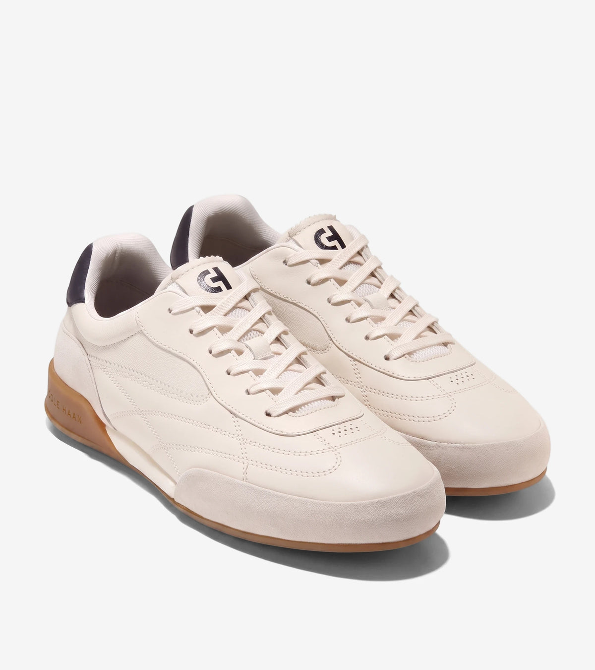 A pair of Cole Haan Grandpro Turf 2.0 sneakers in ivory with silver birch accents and a brown sole, displayed from an angled