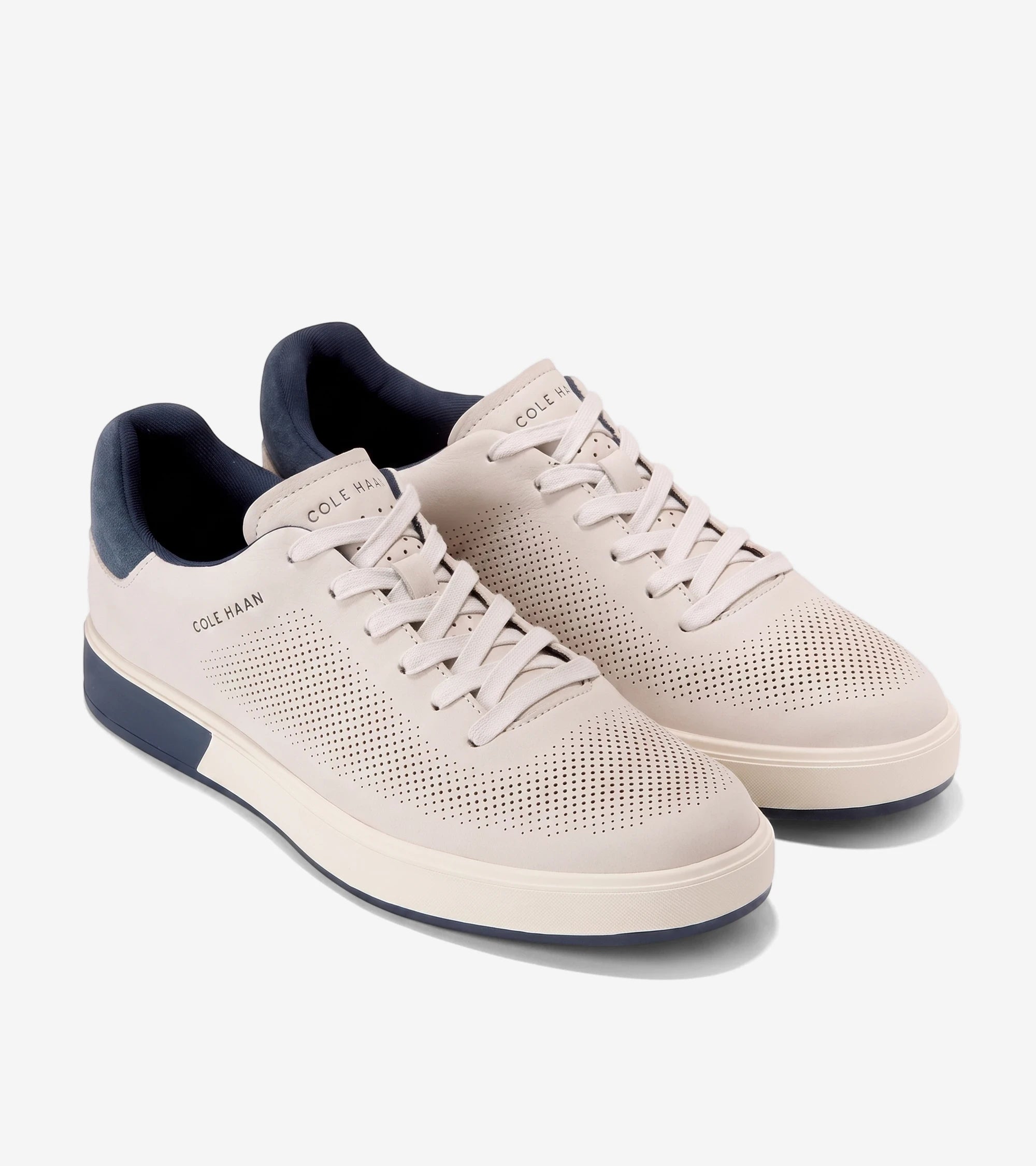 Pair of Cole Haan GP Angleace sneakers in light tan nubuck with navy blue accents and perforated details, angled view.